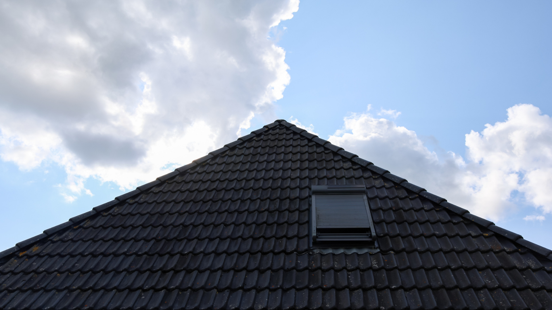 Dark pantile pitched roof with a roof window seen against a blue sky