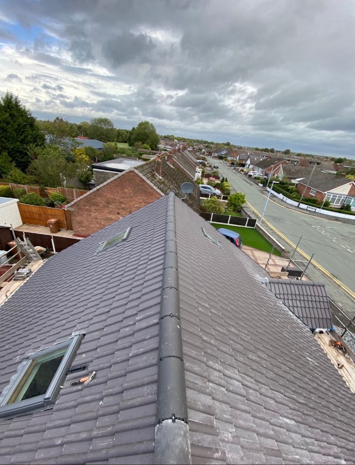 Finished grey tiled pitched roof with dry ridge and roof windows overlooking a residential street