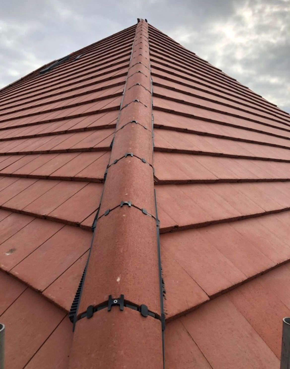 New red clay plain tiled hip and dry ridge system on a freshly finished pitched roof